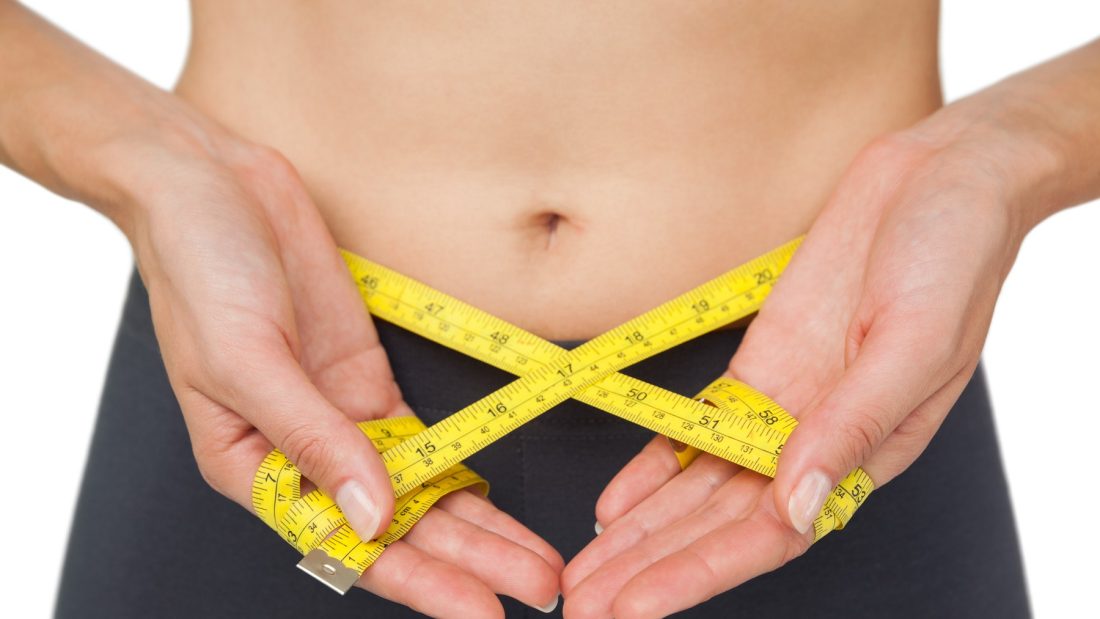 Close-up mid section of a woman measuring waist over white background