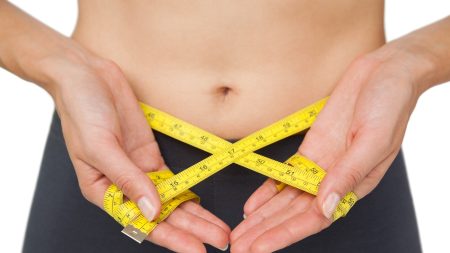 Close-up mid section of a woman measuring waist over white background