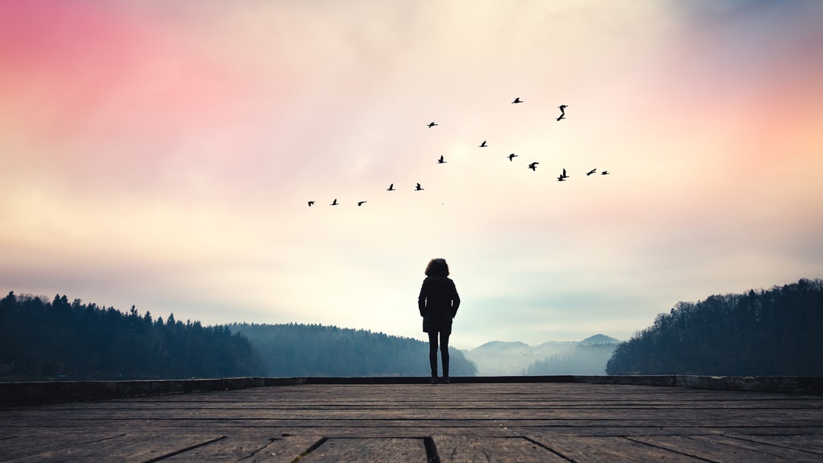 Woman standing on jetty and watching sunrise by the lake.